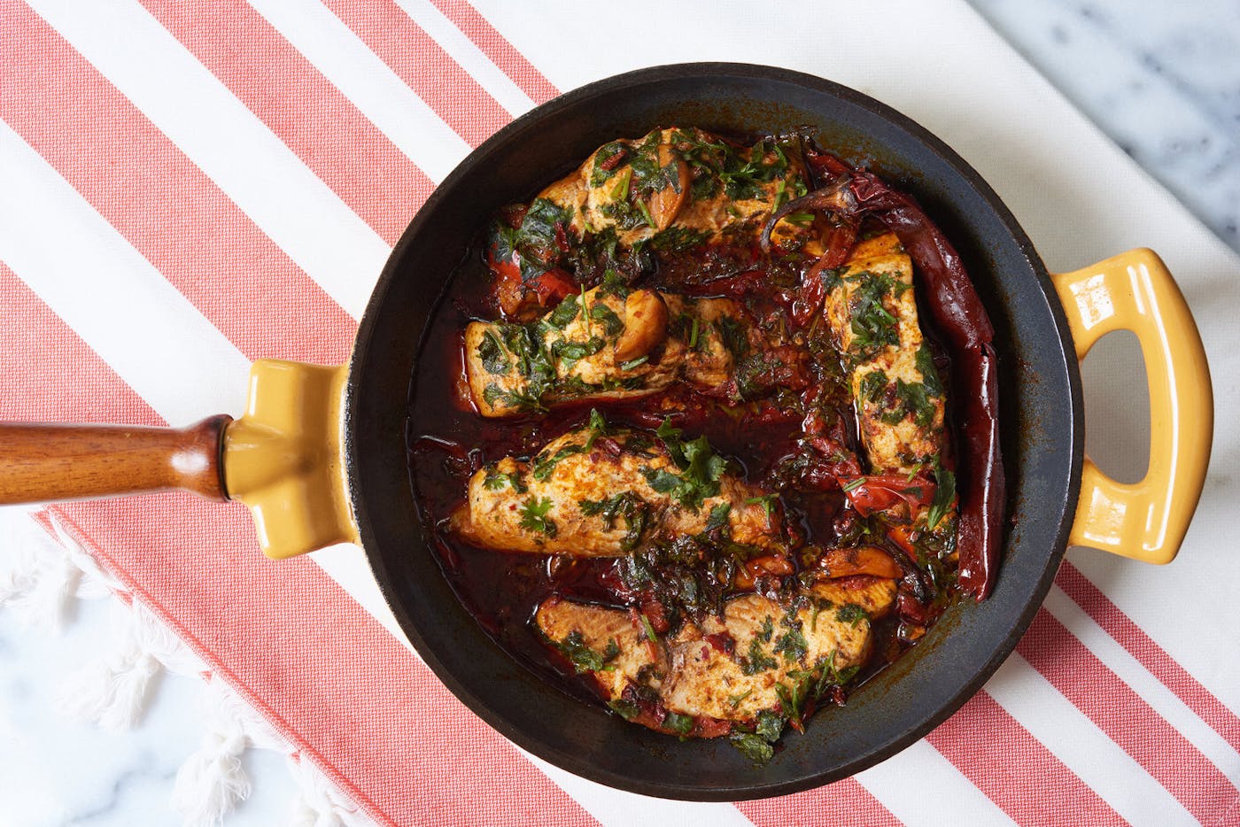 Spicy Moroccan fish in sauce with cilantro and dried guajillo peppers in cast iron skillet.