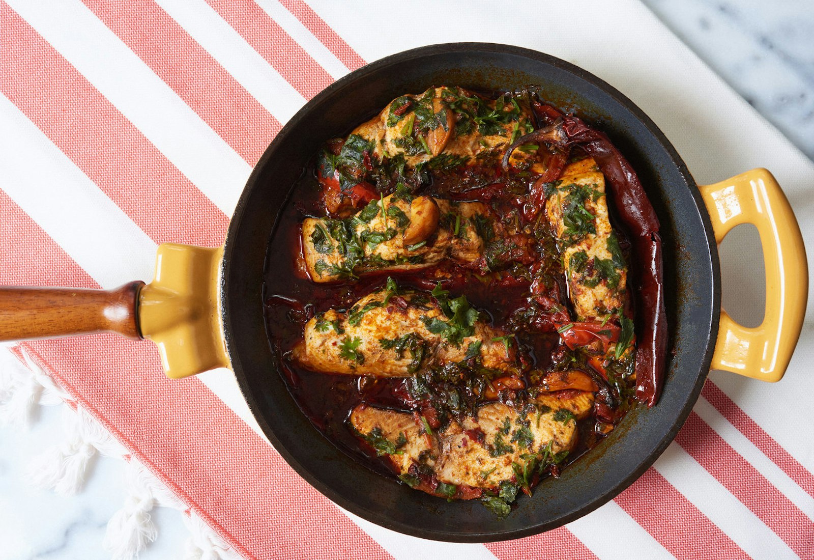Spicy Moroccan fish in sauce with cilantro and dried guajillo peppers in cast iron skillet.