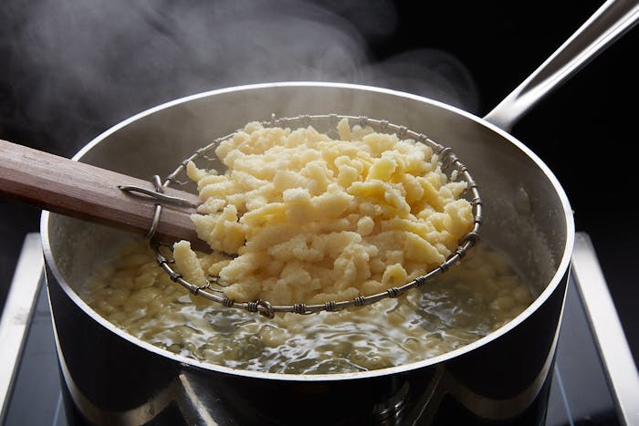 Freshly cooked nokedli held in spider strainer above pot of boiling nokedli.