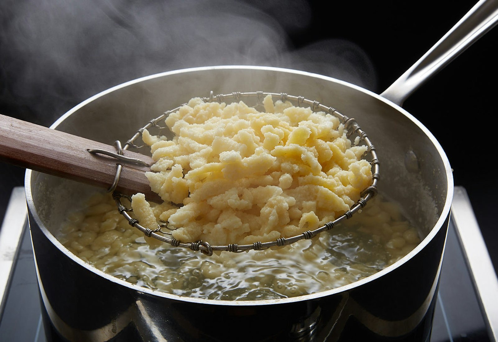 Freshly cooked nokedli held in spider strainer above pot of boiling nokedli.