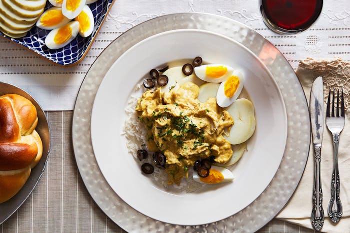 Ají de Gallina served with eggs, potatoes, rice and olives on a white dinner plate.