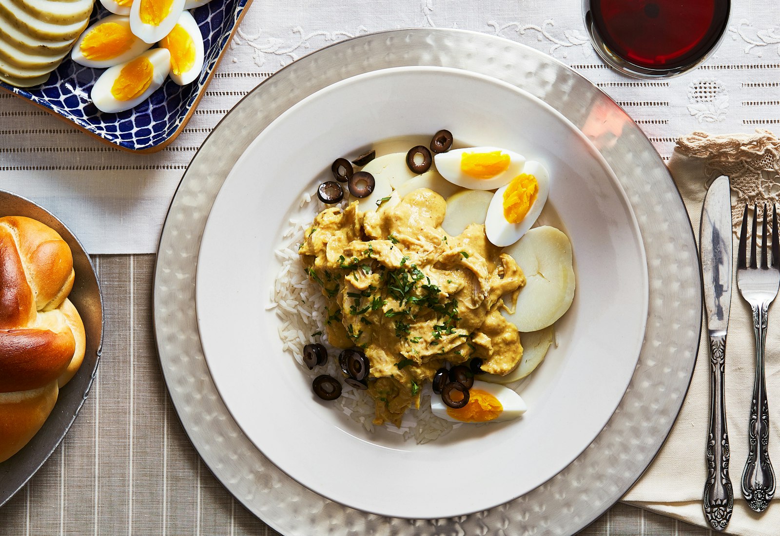 Ají de Gallina served with eggs, potatoes, rice and olives on a white dinner plate.