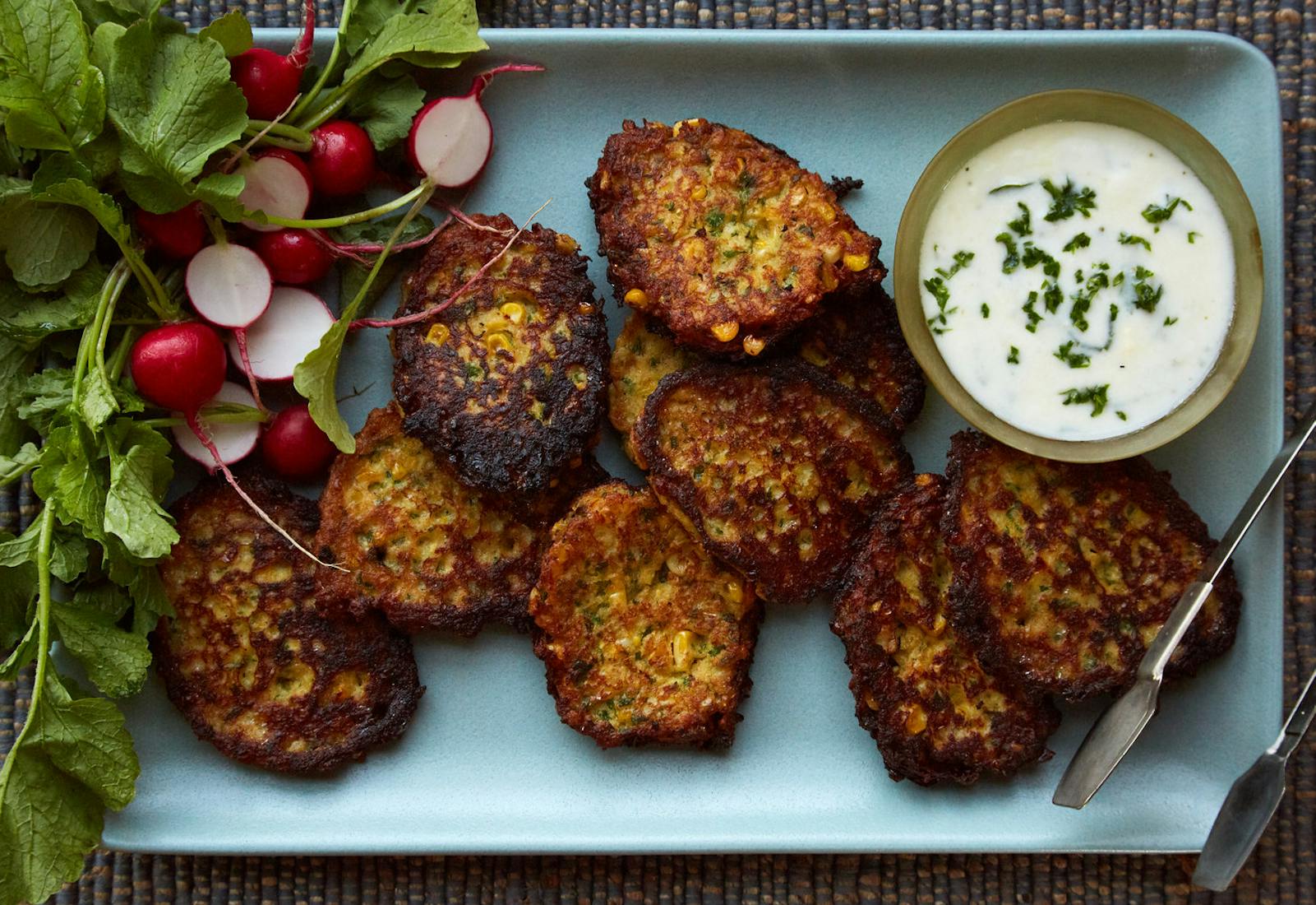 Corn latkes with tzatziki and fresh radishes on blue tray.