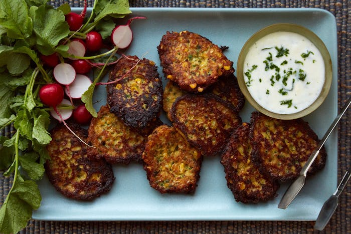 Corn latkes with tzatziki and fresh radishes on blue tray.