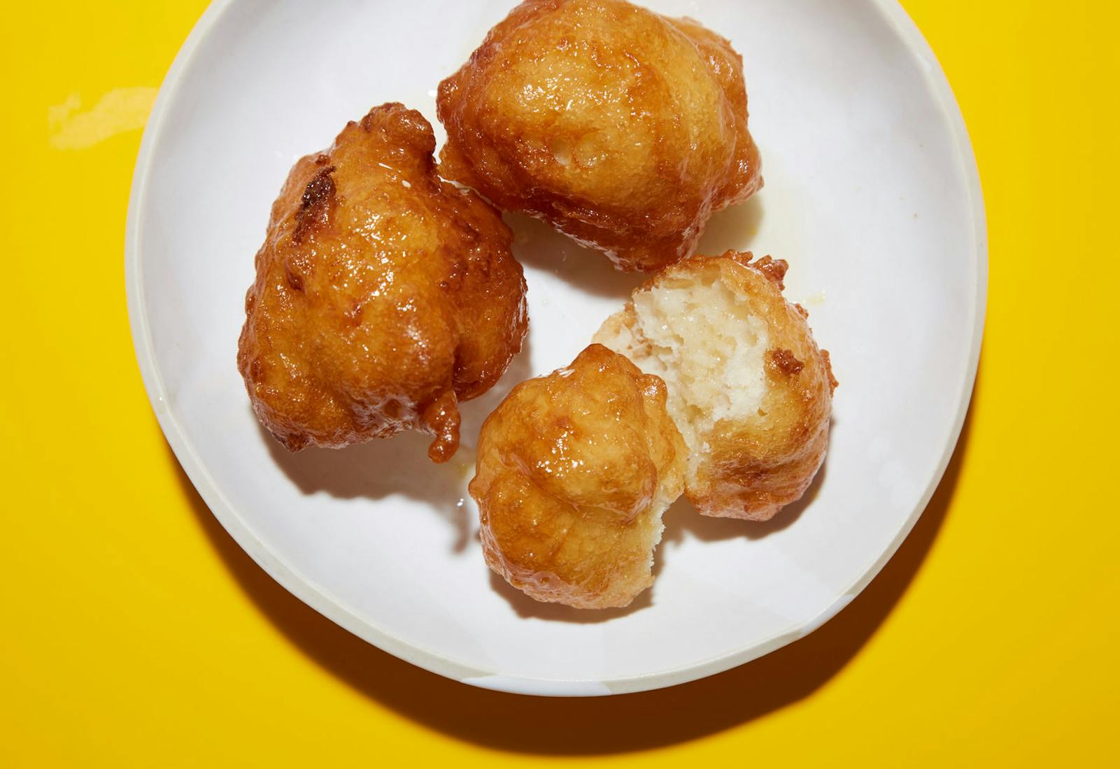 Zalabia coated in honey and orange blossom syrup on white plate atop yellow surface.