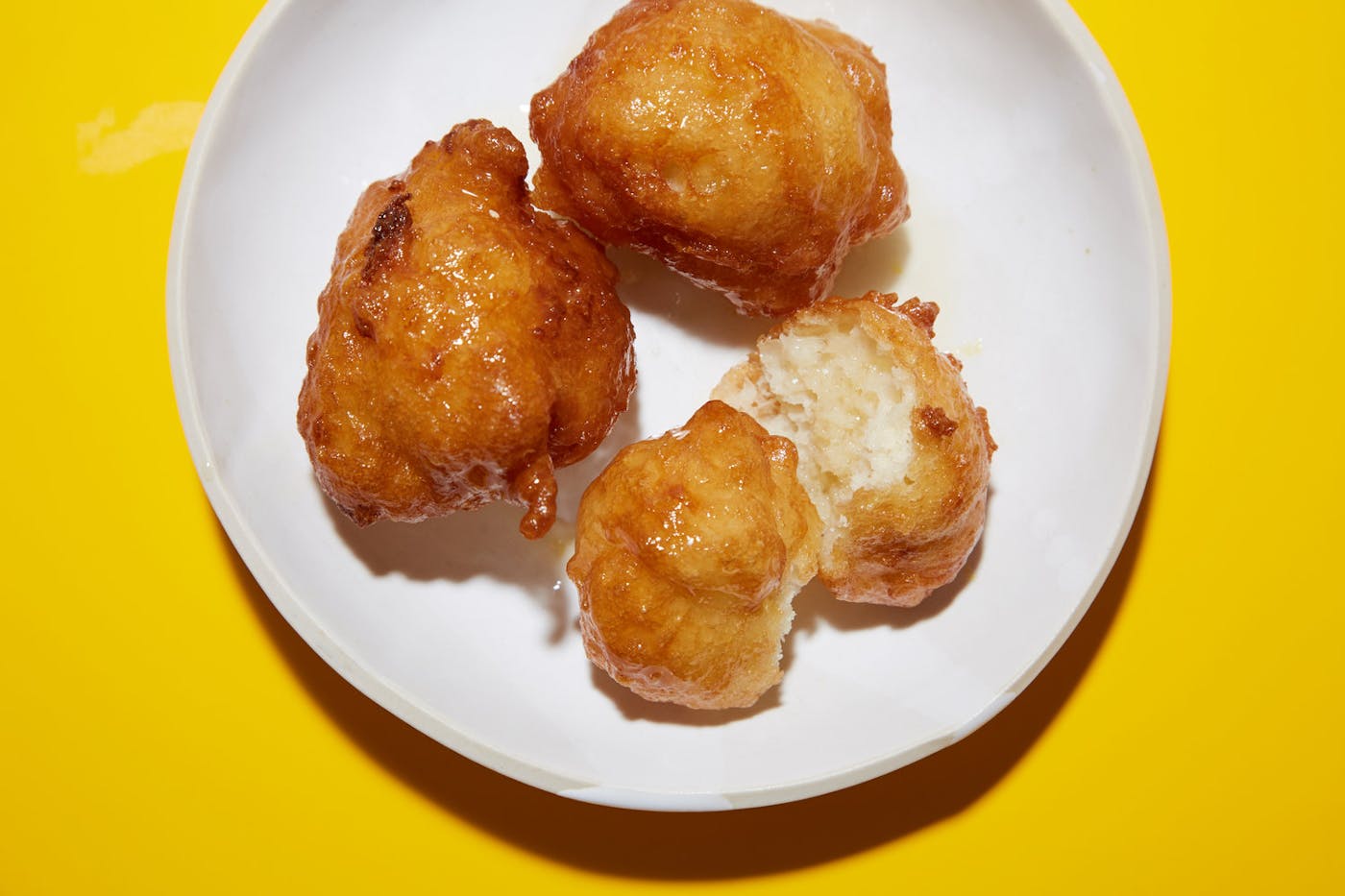 Zalabia coated in honey and orange blossom syrup on white plate atop yellow surface.