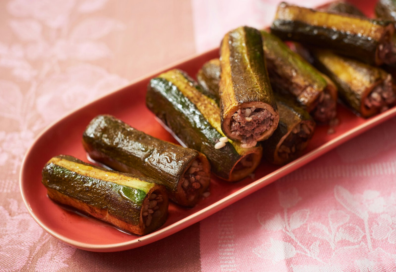 Zucchini mahshi on oblong red dish, atop pink and brown tablecloth.