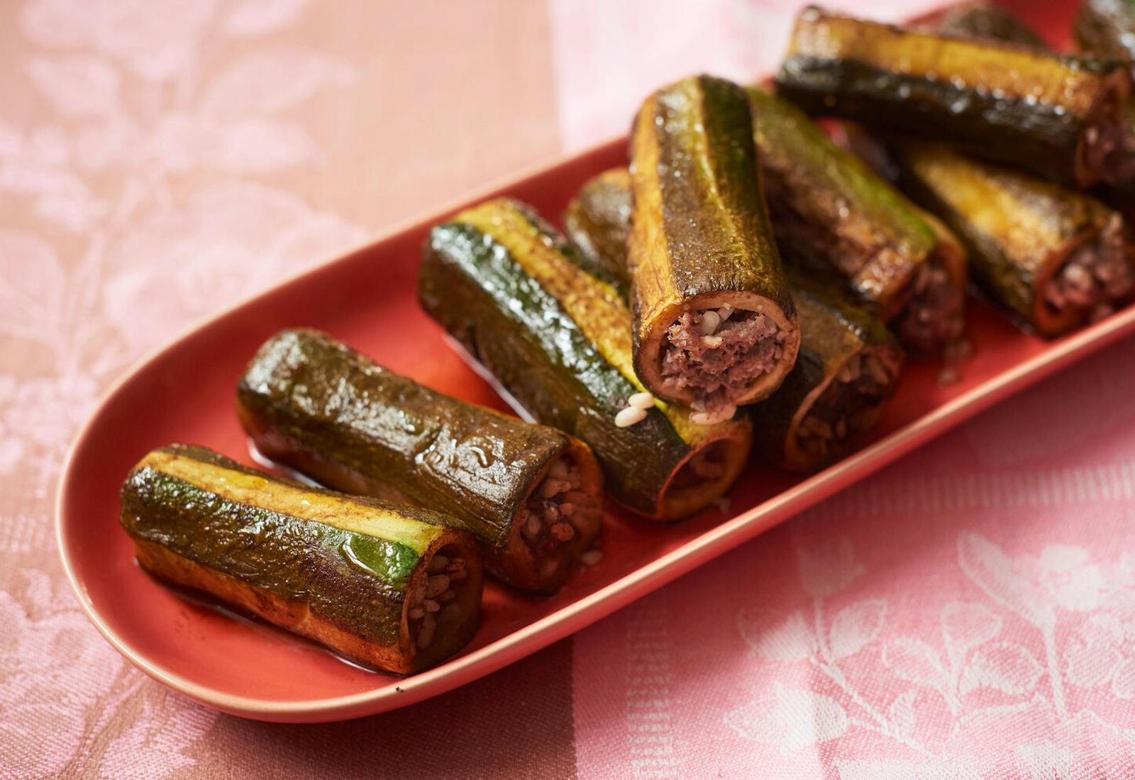 Zucchini mahshi on oblong red dish, atop pink and brown tablecloth.