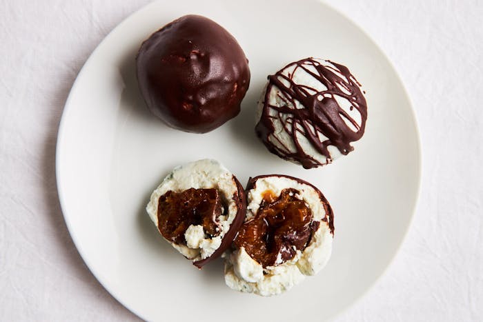 Cheese and chocolate truffles with prunes on white plate atop white surface.
