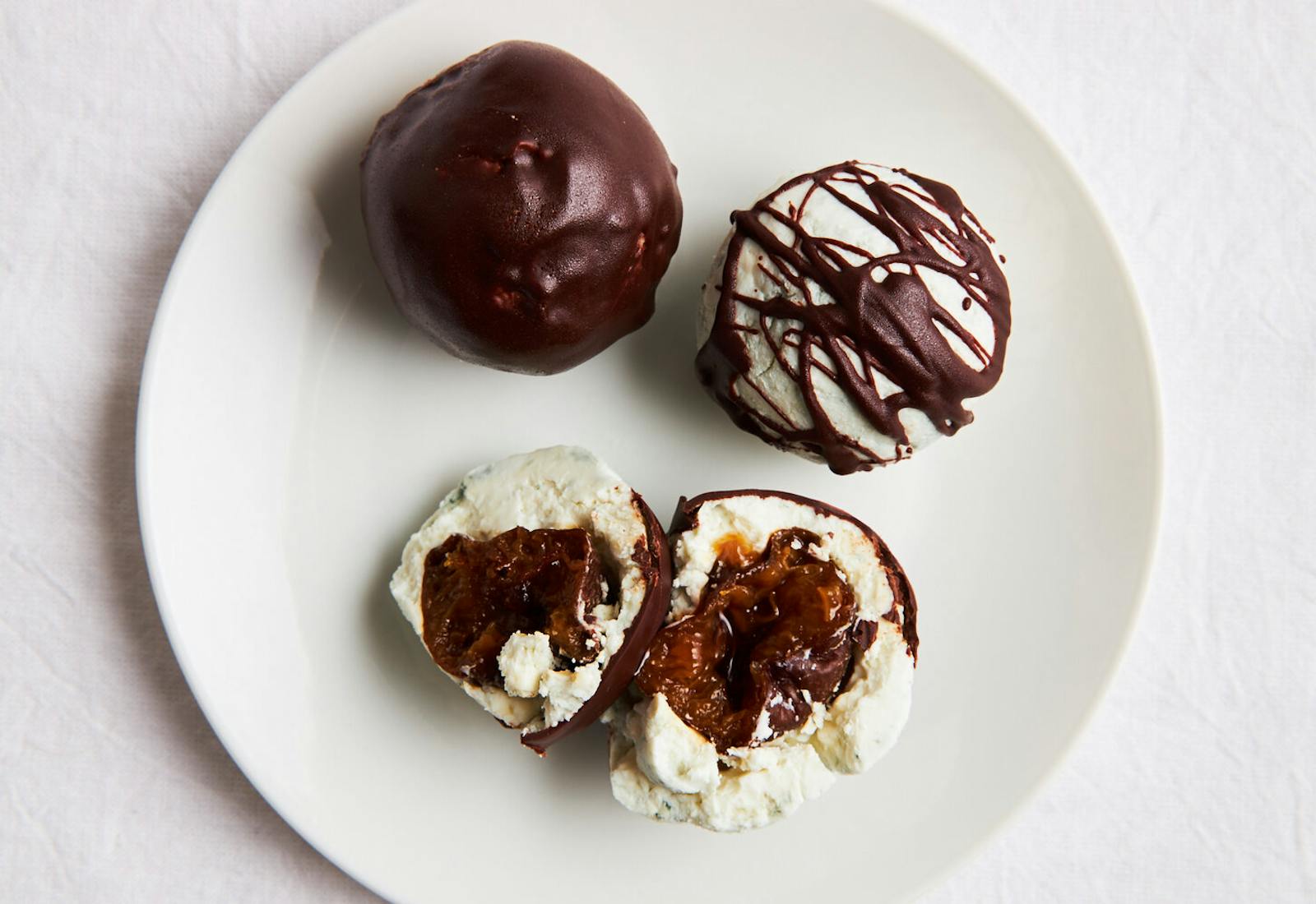 Cheese and chocolate truffles with prunes on white plate atop white surface.