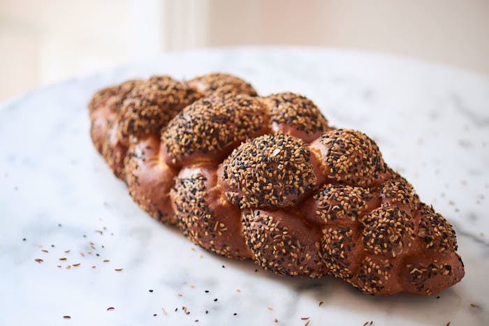 Loaf of seeded sourdough challah on marble table.