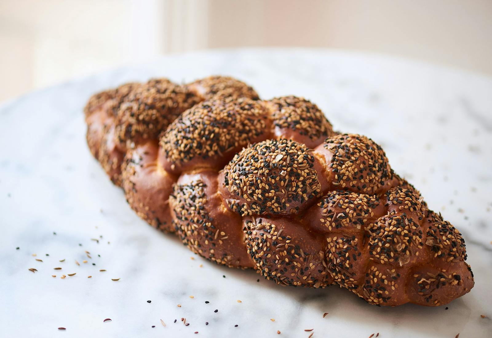 Loaf of seeded sourdough challah on marble table.