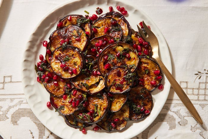 Fried eggplant with mint vinaigrette and pomegranate kernels on white plate atop white patterned tablecloth.