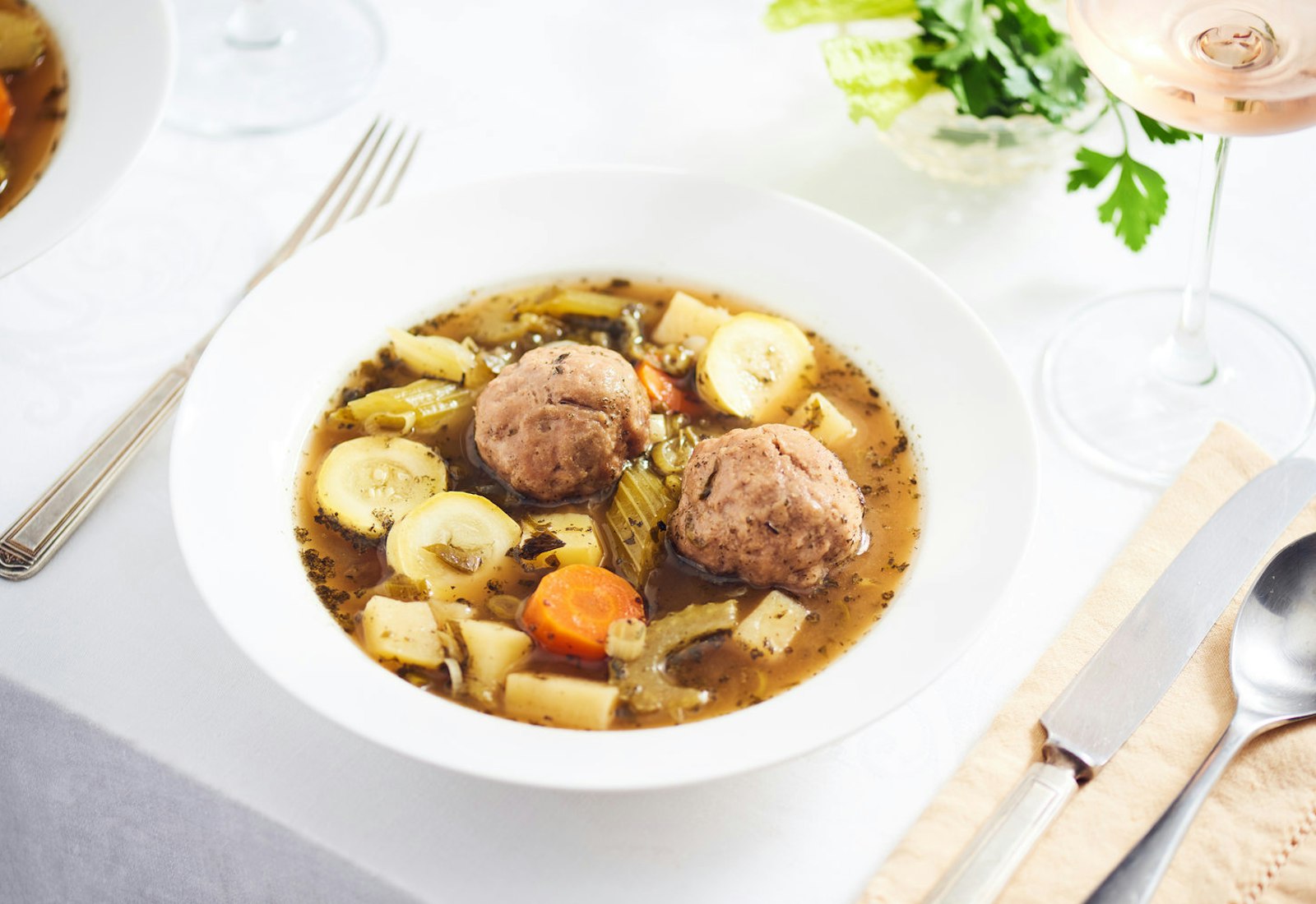 Formal table setting with kibbeh hamdah in white bowl alongside glass of rosé.