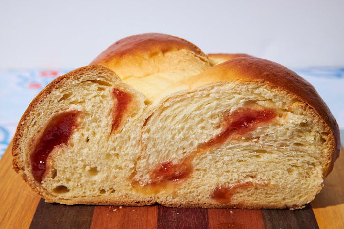 Loaf of guava challah sliced in half atop wood cutting board.