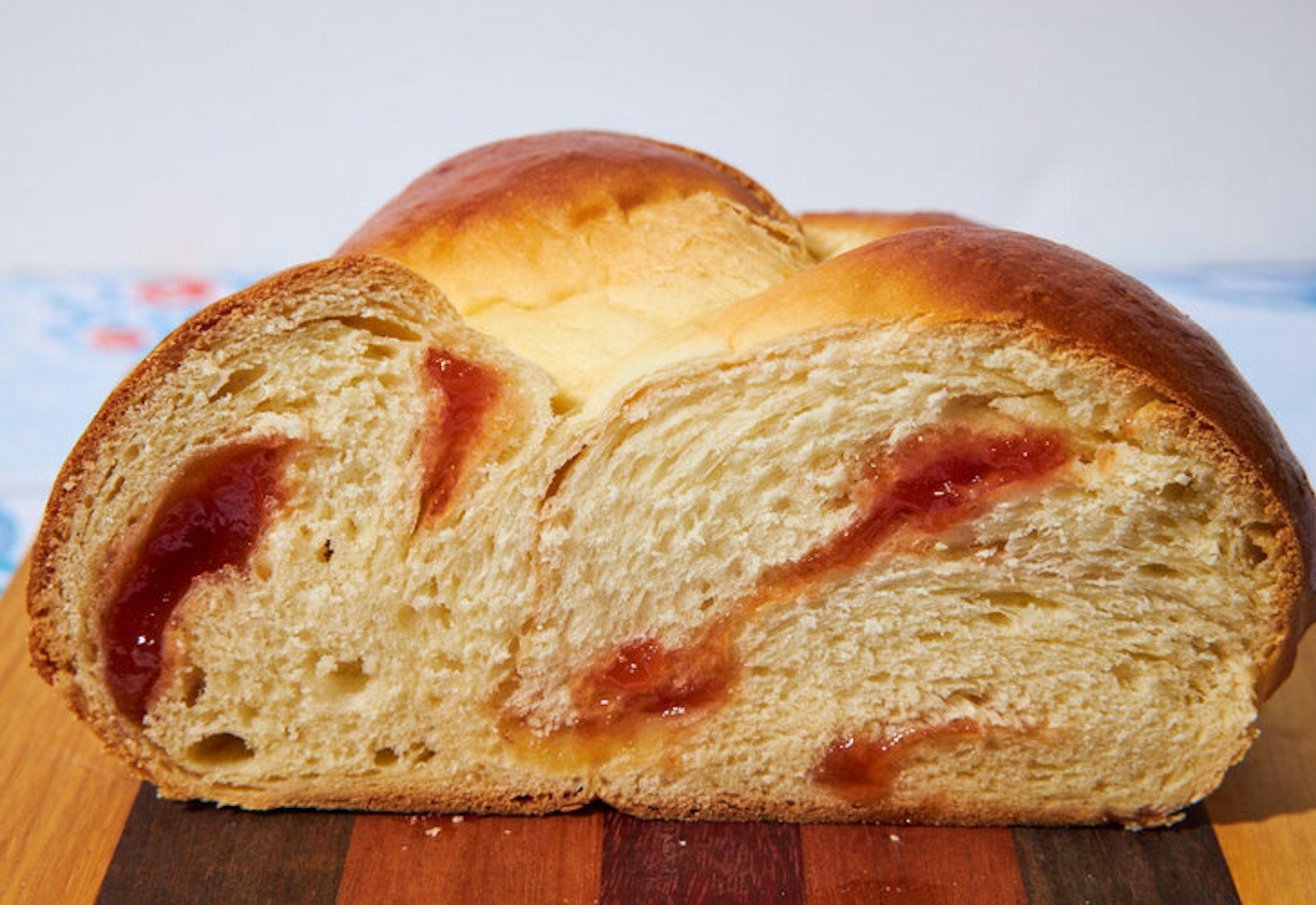 Loaf of guava challah sliced in half atop wood cutting board.