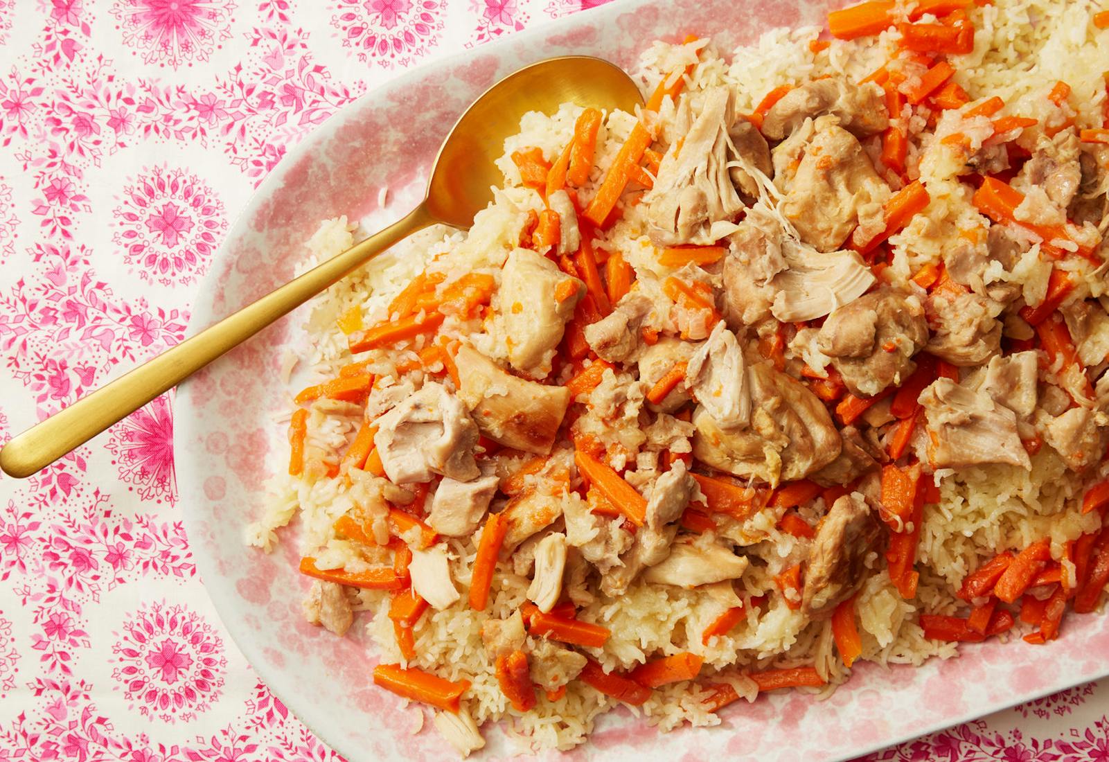 Plov in dish with pale pink flowers atop pink tablecloth.