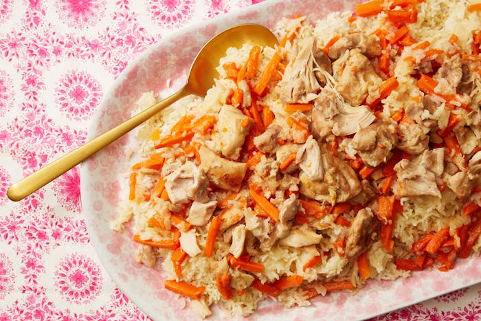 Plov in dish with pale pink flowers atop pink tablecloth.