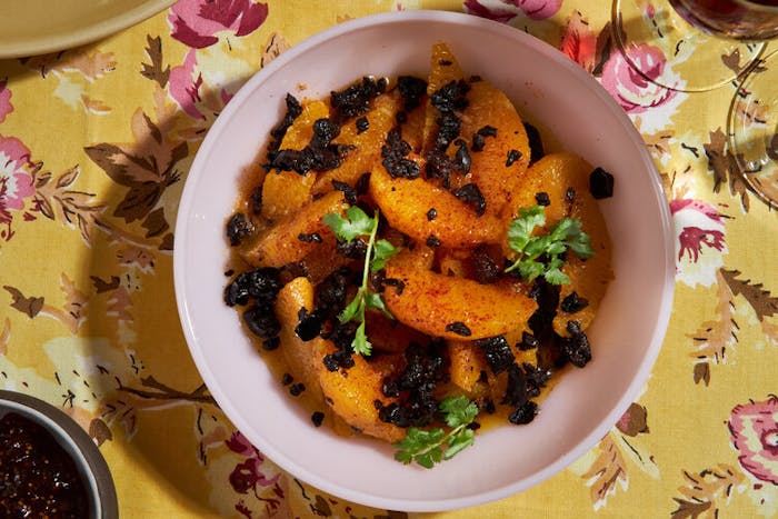 Orange and olive salad with sprigs of cilantro atop yellow floral tablecloth.