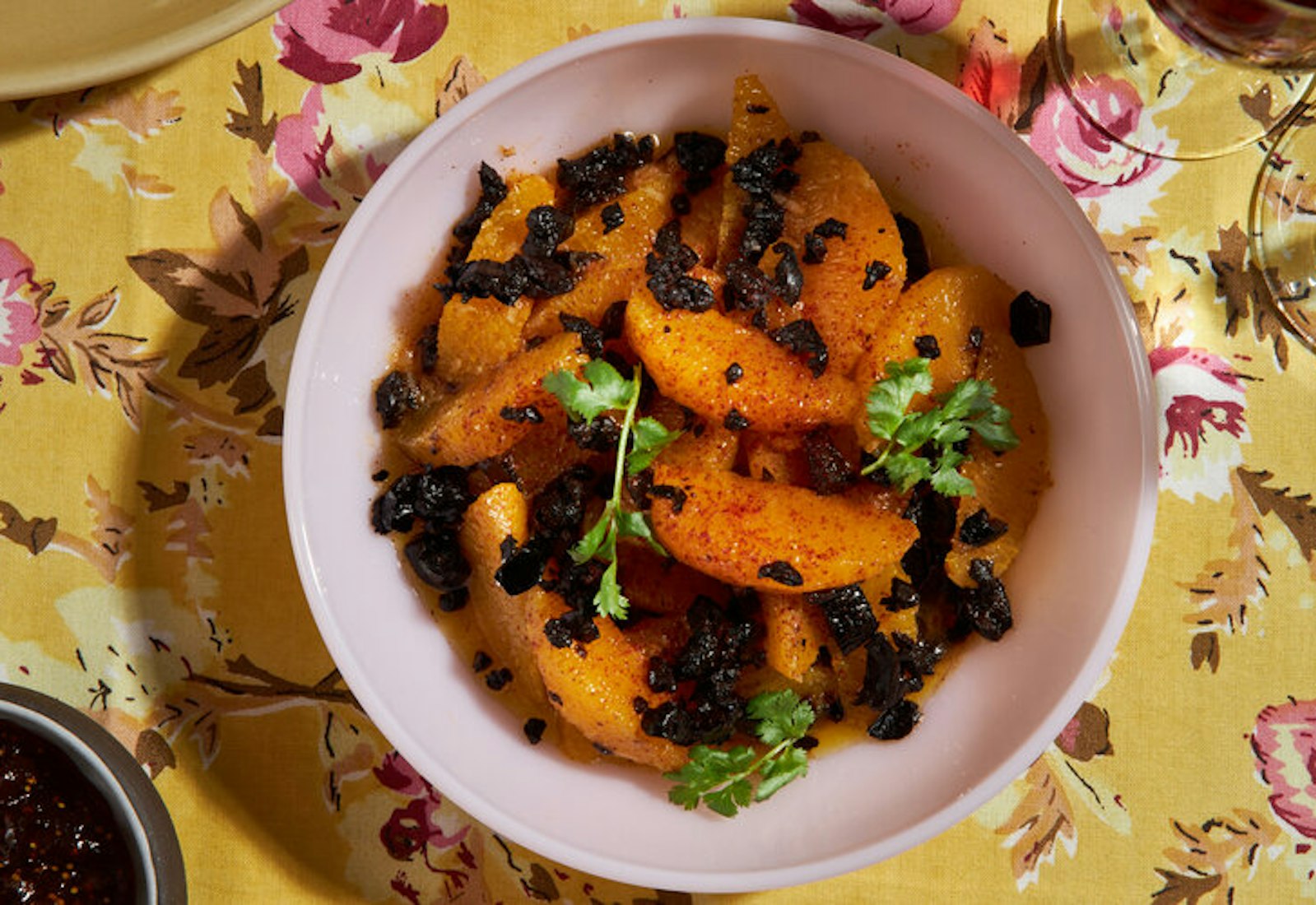 Orange and olive salad with sprigs of cilantro atop yellow floral tablecloth.