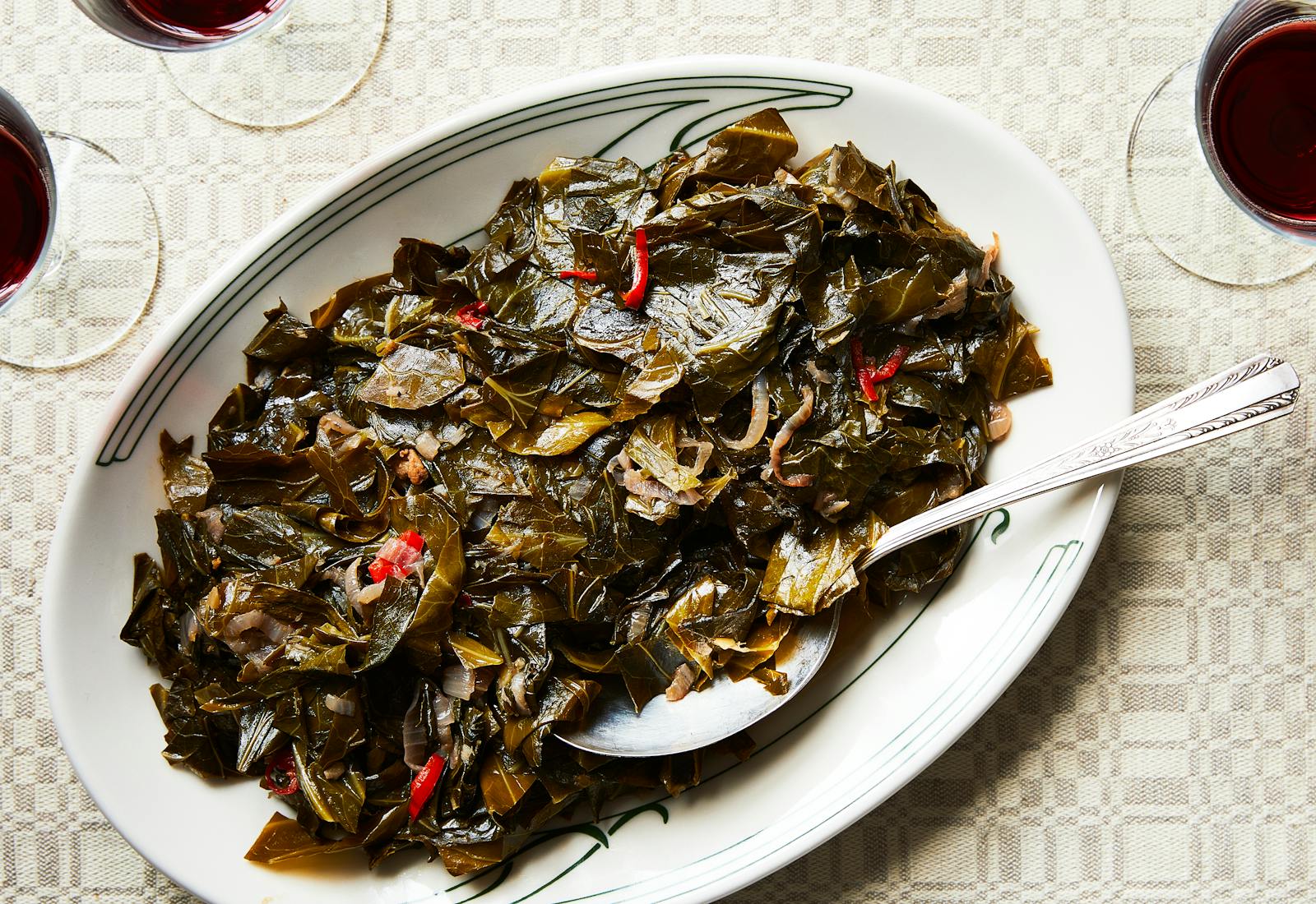 Braised collards on white serving platter with serving spoon.