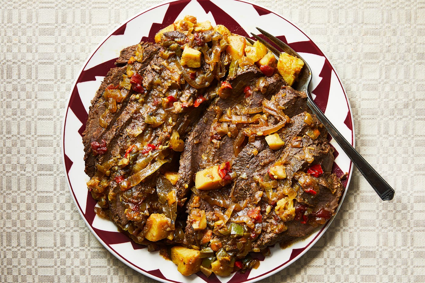 Sliced brisket served with sauce on red and white serving plate.