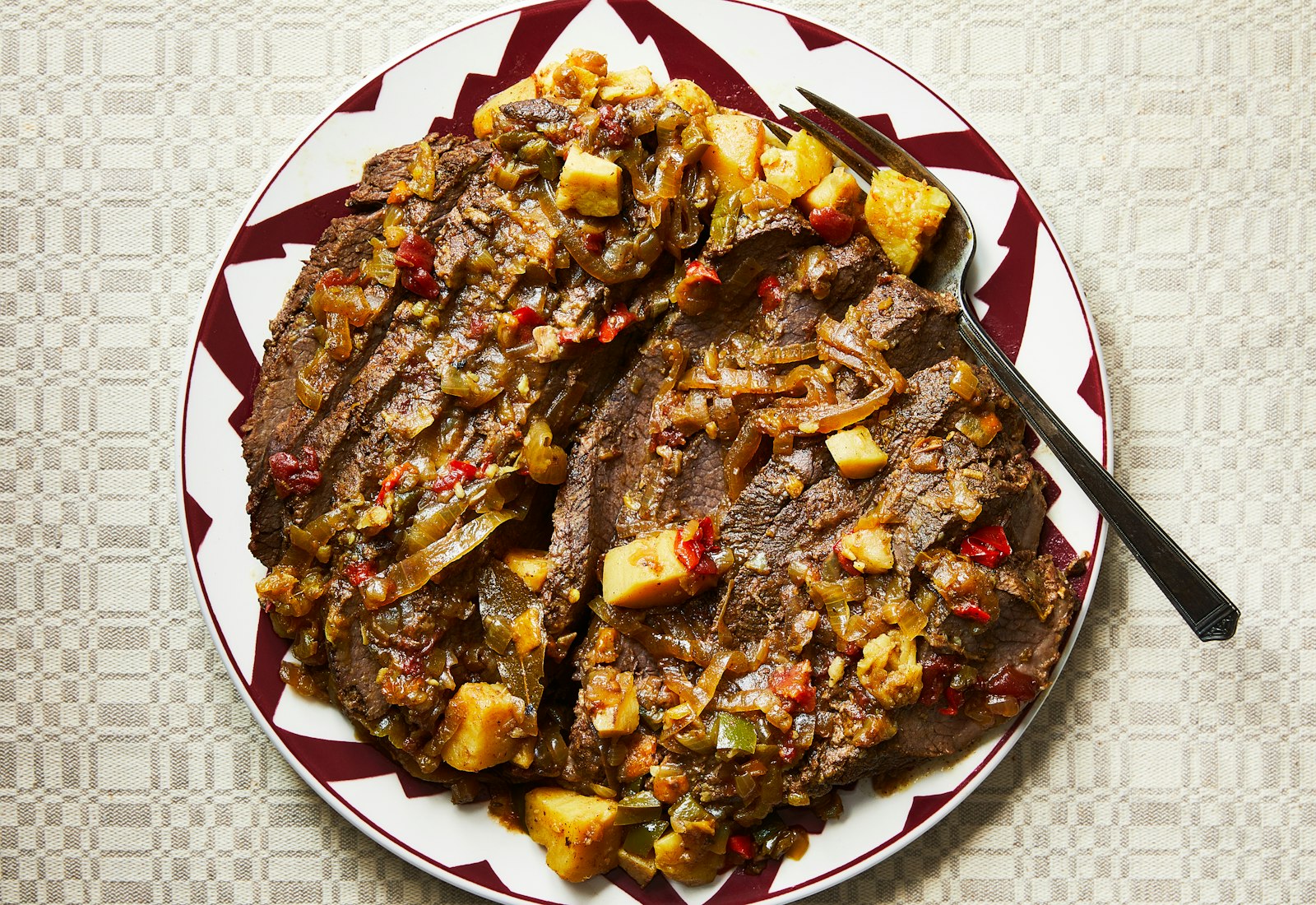 Sliced brisket served with sauce on red and white serving plate.
