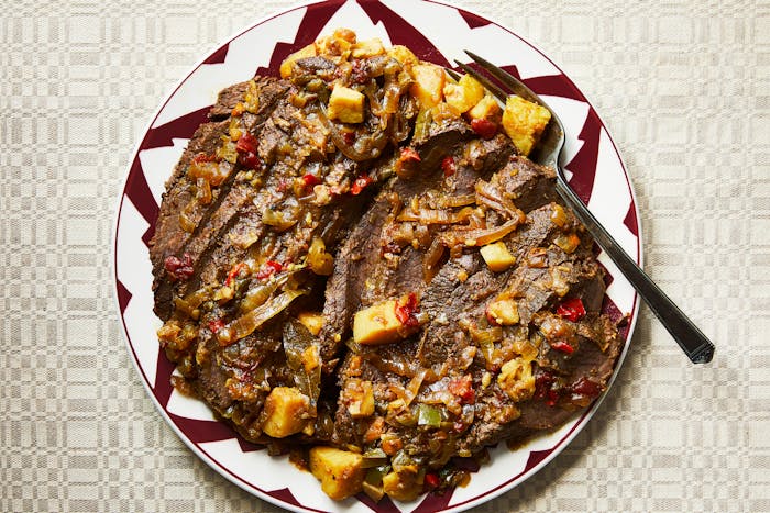 Sliced brisket served with sauce on red and white serving plate.