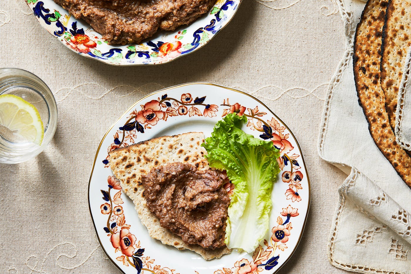 Haroset spread on piece of matzah next to green lettuce leaf or dinner plate.