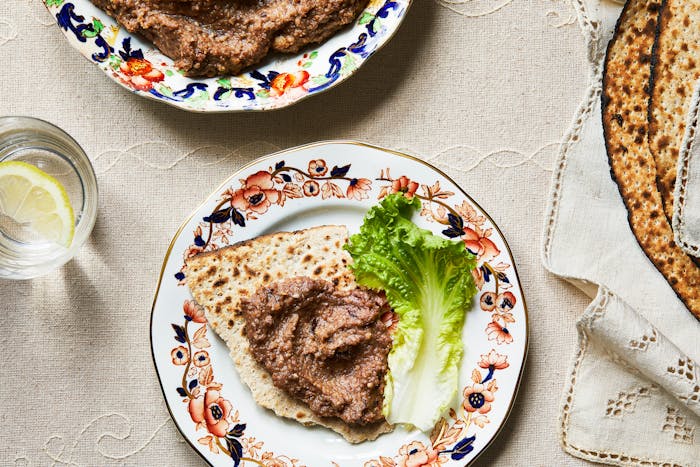 Haroset spread on piece of matzah next to green lettuce leaf or dinner plate.