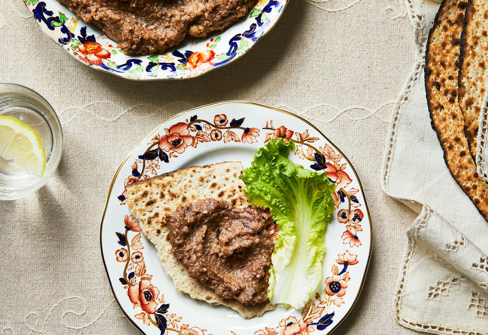 Haroset spread on piece of matzah next to green lettuce leaf or dinner plate.