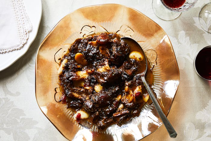 Oxtail stew served in large, glass amber bowl atop white floral tablecloth.