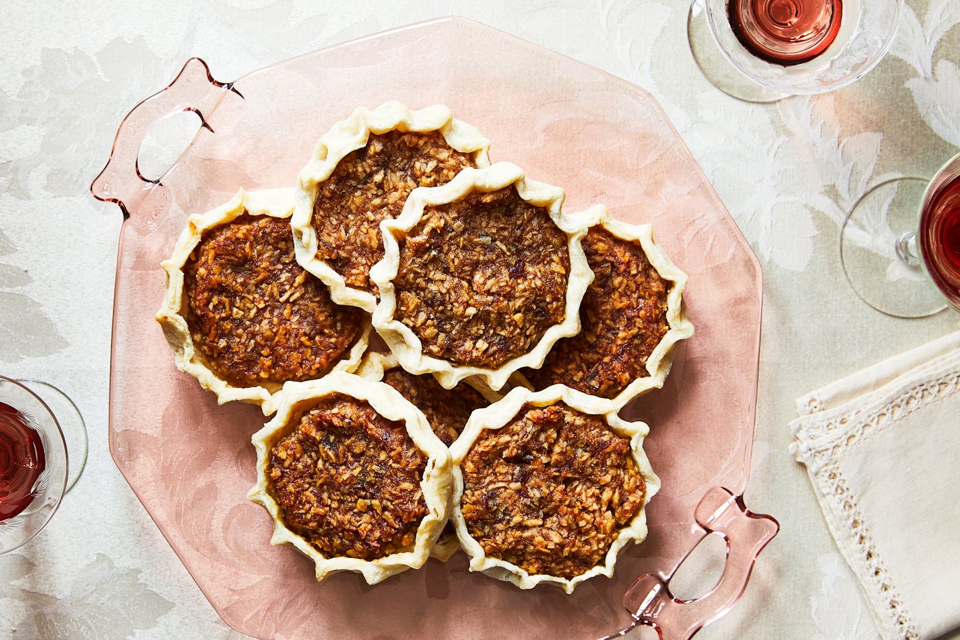 Gizzada tartlets served on light pink platter atop white floral tablecloth.