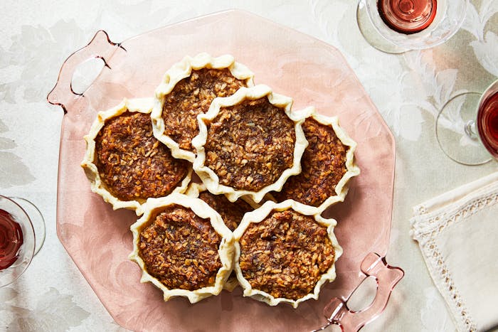 Gizzada tartlets served on light pink platter atop white floral tablecloth.