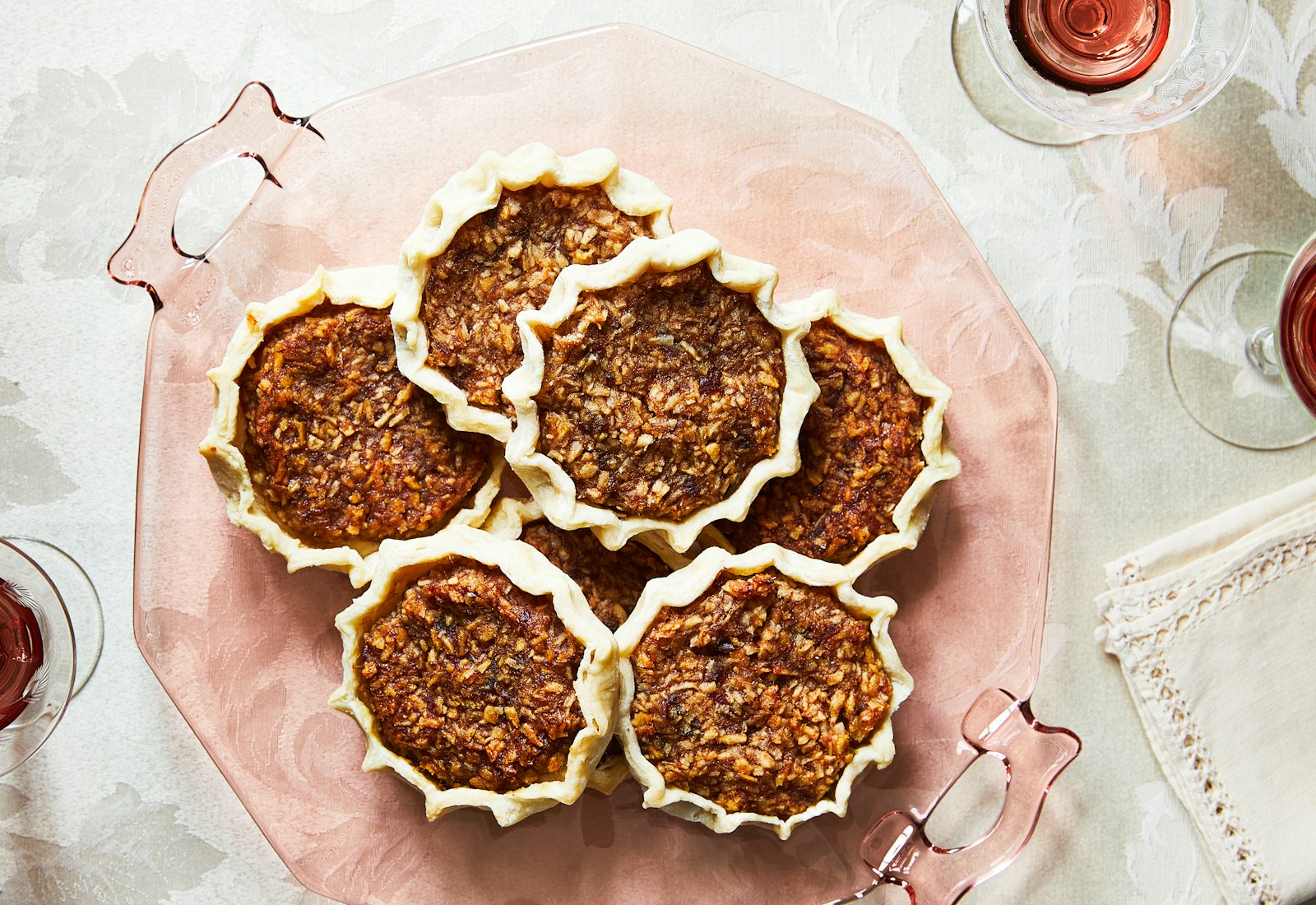 Gizzada tartlets served on light pink platter atop white floral tablecloth.