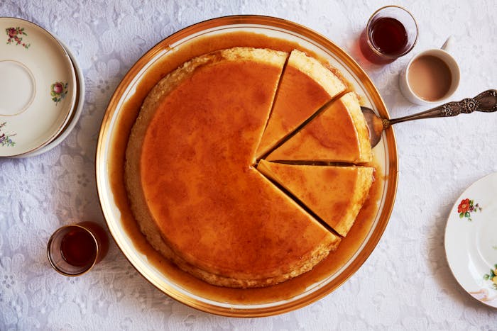 Creme caramel with three slices and cake server atop white, lace tablecloth.