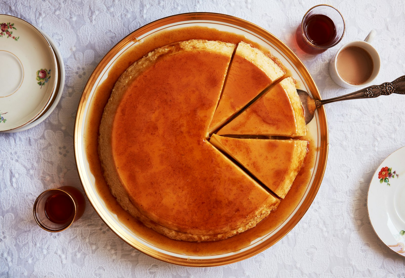 Creme caramel with three slices and cake server atop white, lace tablecloth.