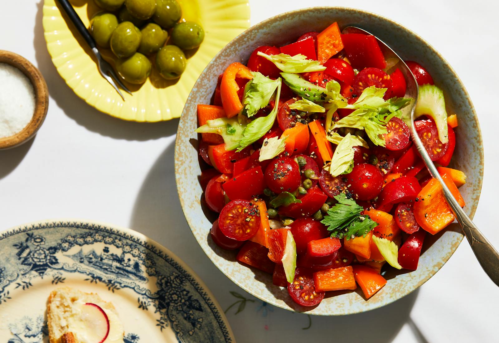 Chopped salad in serving bowl alongside green olives and small bowl of salt.