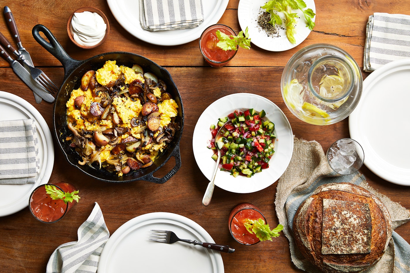 Tablespread with scrambled eggs with sauteed mushrooms and onions in cast iron, cucumber tomato salad, bloody Miriams and a loaf of bread.