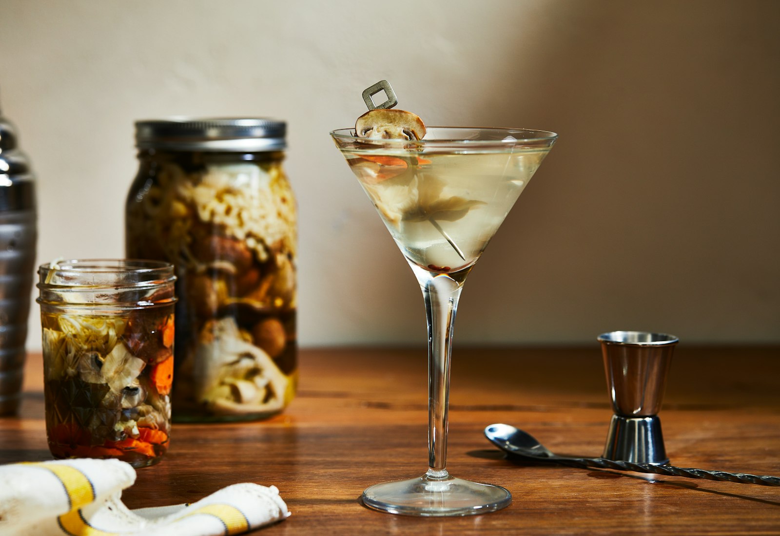 Pickled mushroom martini in martini glass atop dark wood table.