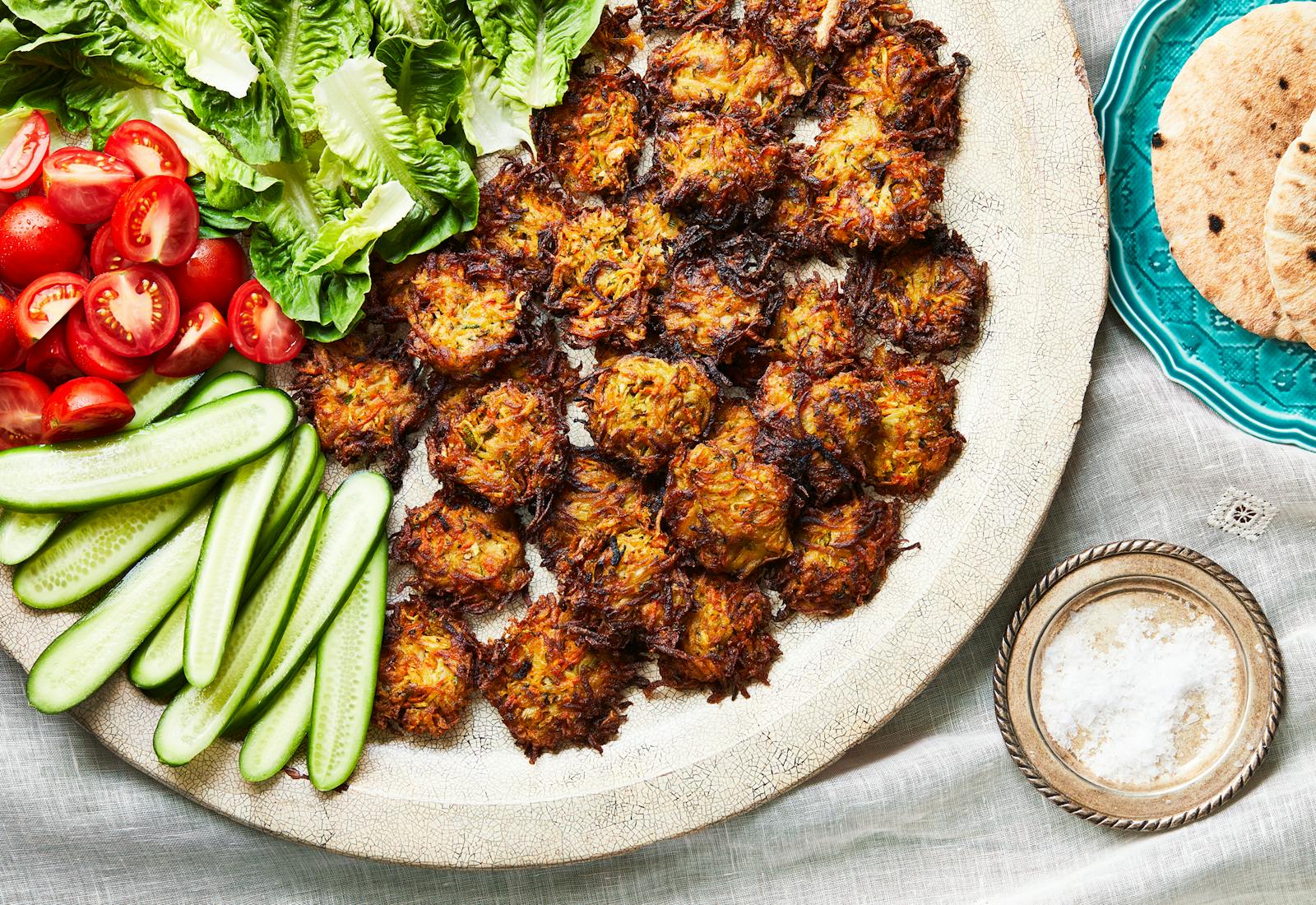 A large platter features small round vegetable fritters and an assortment of fresh vegetables. 