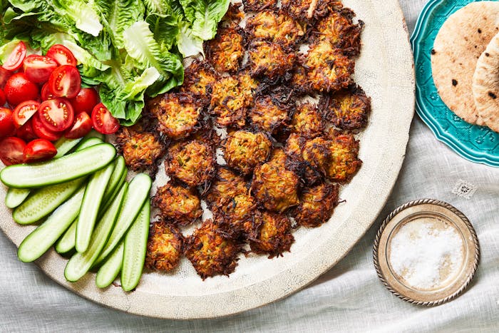 A large platter features small round vegetable fritters and an assortment of fresh vegetables. 