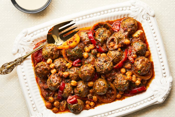 Spiced Morroccan fish patties are served on a square tray with a sauce of chickpeas, peppers and tomatoes.