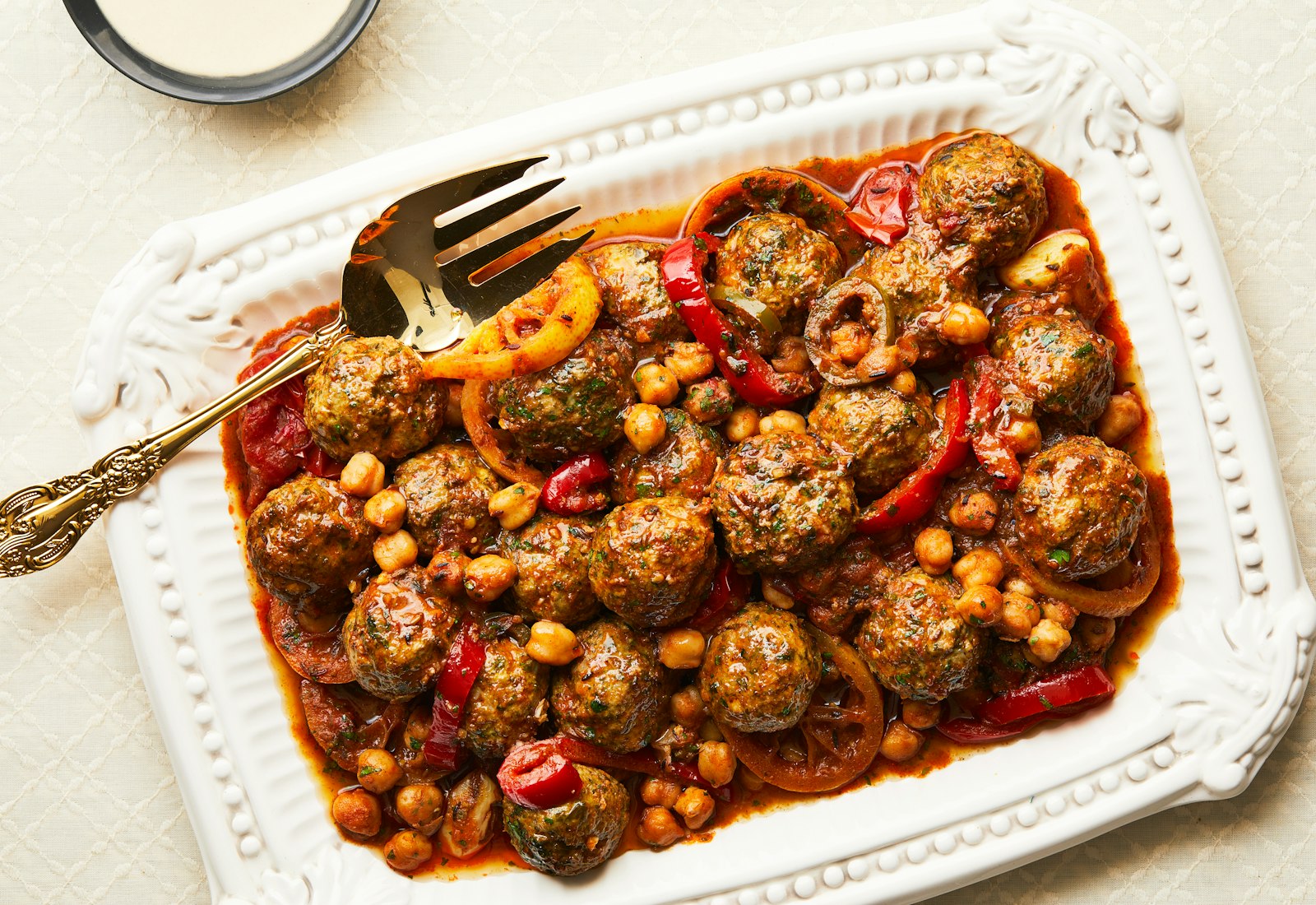 Spiced Morroccan fish patties are served on a square tray with a sauce of chickpeas, peppers and tomatoes.