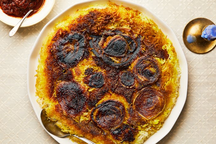 Spiced yellow rice featuring a layer of crispy onions on top, with a small bowl of matbucha and a candle in the corner.