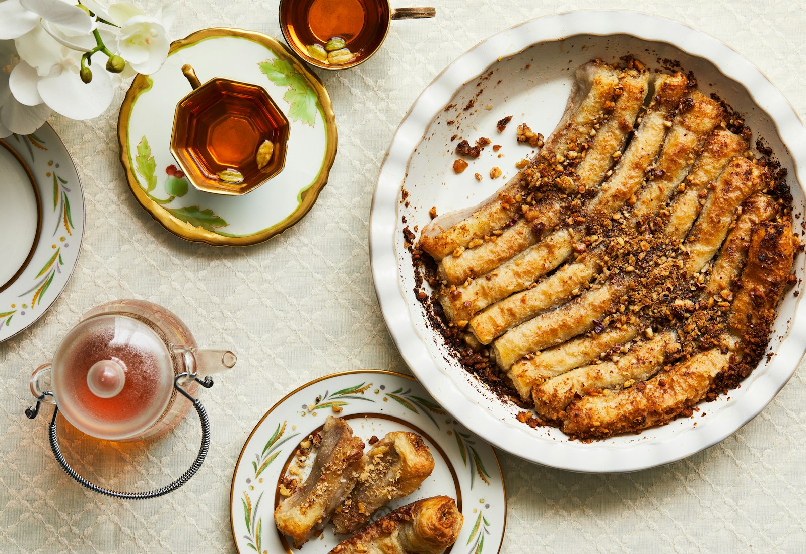 Iraqi Baklava Cigars with crushed nuts and orange blossom syrup in a round pie dish, with pieces on a plate.