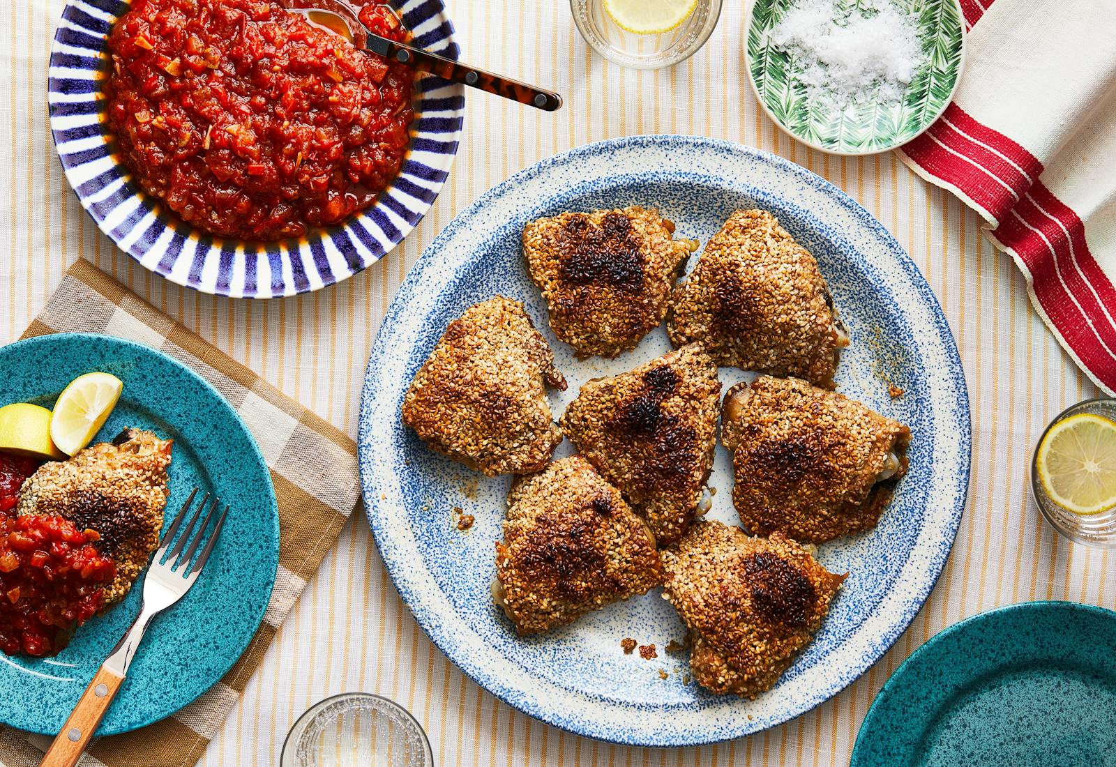 Crispy sesame chicken thighs with a pinch bowl of flaky salt and a bowl of matbucha. 