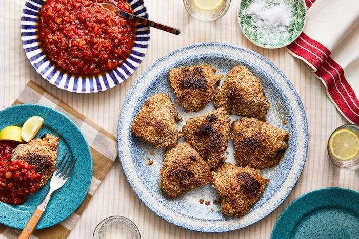 Crispy sesame chicken thighs with a pinch bowl of flaky salt and a bowl of matbucha.
