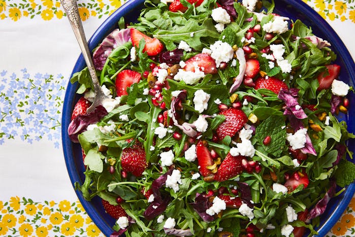A colorful radicchio and arugula salad with strawberries, feta, pistachios and pomegranate on a striped tablecloth.