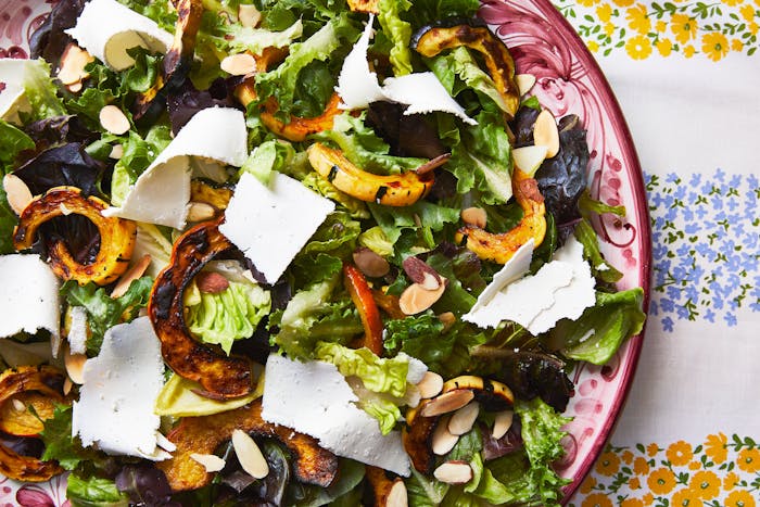 A bowl of colorful salad greens with roasted squash and ricotta salata on a printed tablecloth. 